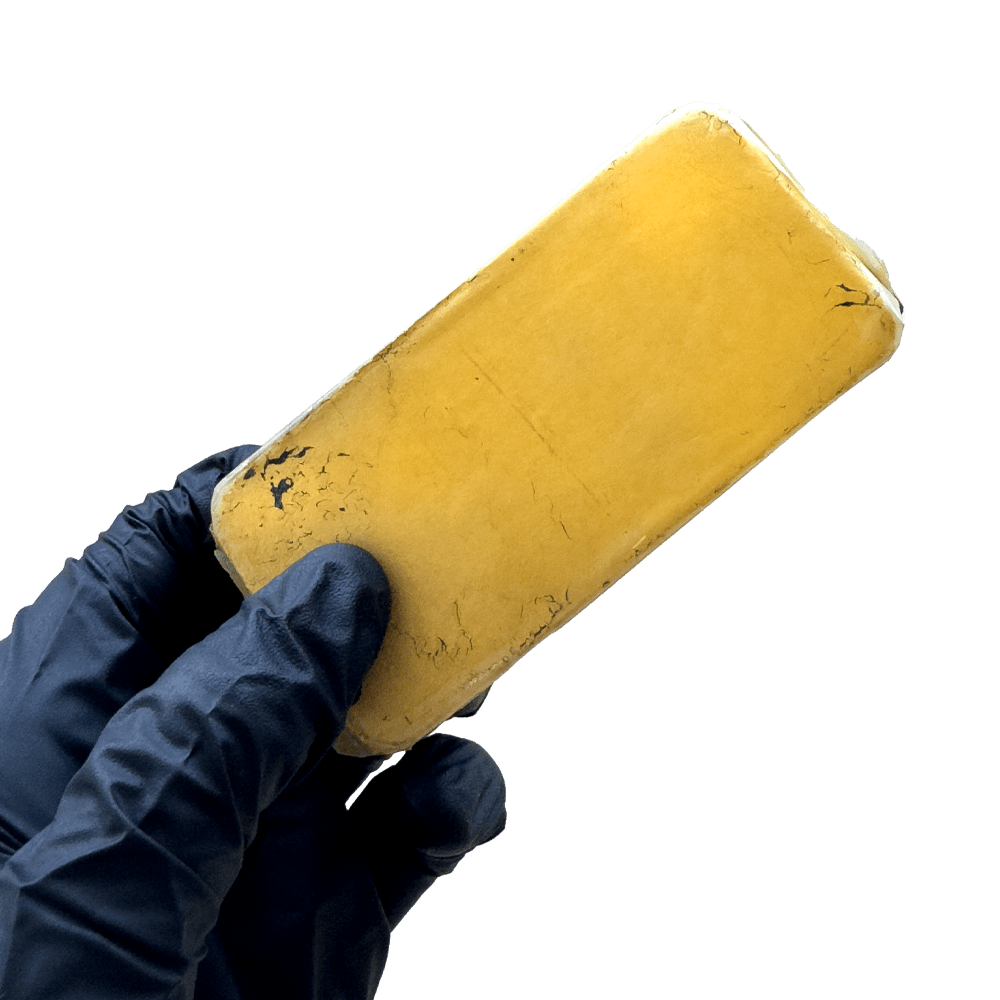 Main tenant le HASCHICH CBD Afghan Gold doré de I LOVE POT, un produit compact à la texture naturelle sur fond blanc.